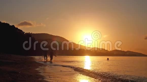 快乐的一对夫妇牵着手在热带海滩上在令人惊叹的日落中缓慢地奔跑1920x1080视频的预览图