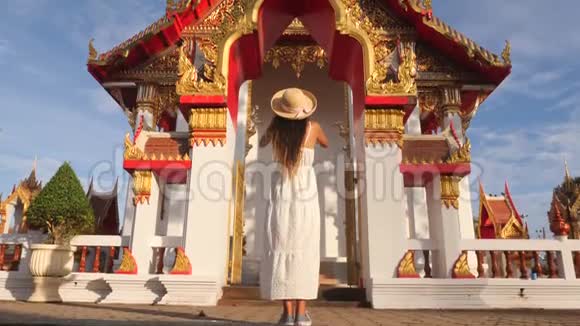 穿着白色连衣裙和大草帽的年轻旅游女孩用泰国佛教寺庙的手机拍照普吉岛视频的预览图