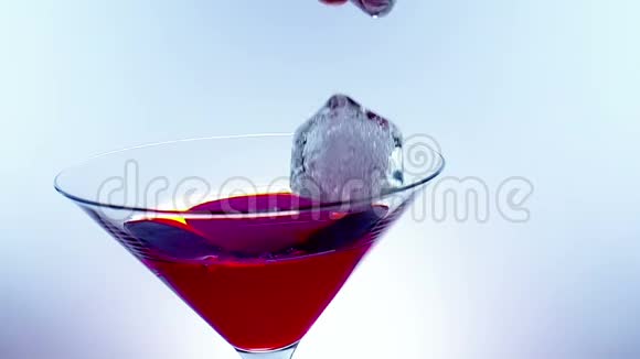 冰块随着溅入红色鲜酒精鸡尾酒在蓝光色调背景下拍摄慢动作视频的预览图