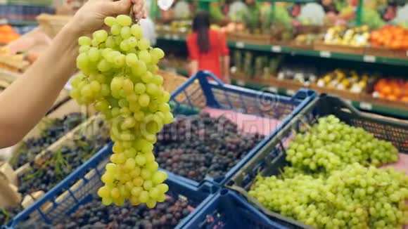 一个女人在蔬菜货架上的超市里买蔬菜和水果人选择绿葡萄慢动作4k视频的预览图