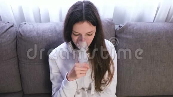 使用雾化器和吸入器进行治疗坐在沙发上的年轻女人通过吸入器面罩吸入视频的预览图