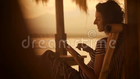 巴厘岛的日落和海滩晚上穿着条纹衬衫和宽裤子的女孩坐在柔软的衣服上视频的预览图