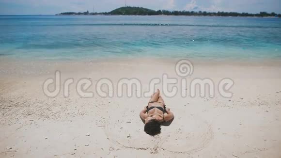 巴厘岛的海滩穿着黑色泳衣的女孩躺在沙滩上休息它舒缓的沙滩视频的预览图