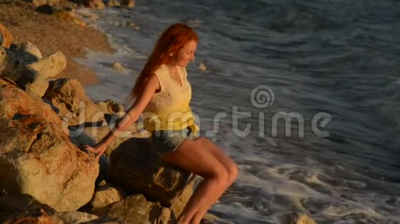 坐在亚得里亚海多岩石的海滩上头发飞扬的年轻女子视频的预览图