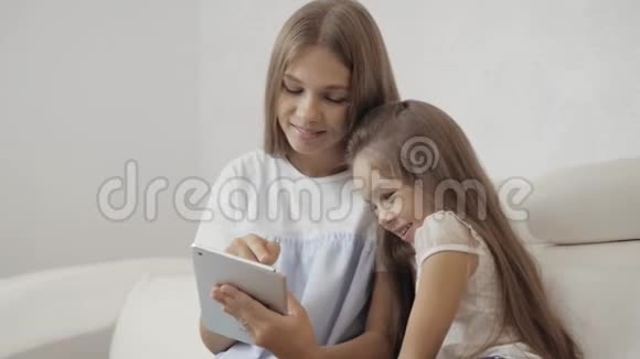 两个姐姐看着平板电脑坐在沙发上玩游戏小婴儿和成年妹妹视频的预览图