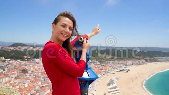 女游客在高山上用硬币付费望远镜观看葡萄牙拿撒勒的城市景观视频的预览图