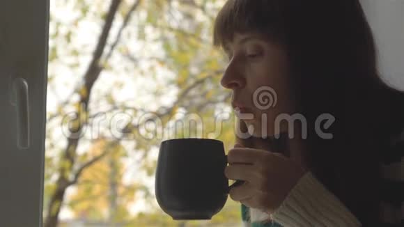 女孩喝了一杯热饮窗外有黄叶的树视频的预览图