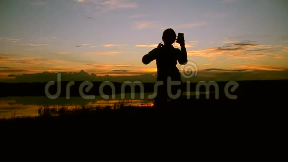 在日落时分在水里拍自拍手机的女孩视频的预览图