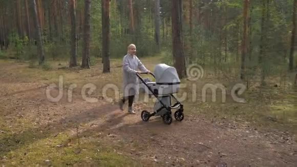 年轻可爱的妈妈带着婴儿车在公园里散步听音乐和跳舞视频的预览图