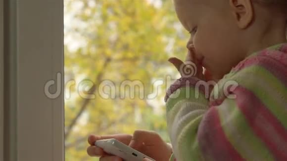 穿着条纹毛衣的小女孩坐在窗台上打电话视频的预览图