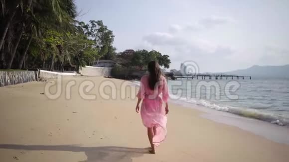 美丽的女性穿着一件长着粉红色连衣裙在岩石上的海滩上走来走去特写镜头4k视频的预览图