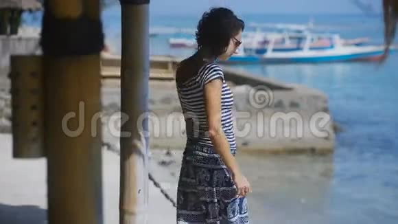 美丽的黑发女郎在海洋上的一个混凝土码头上年轻女子把她的头发和太阳镜系直站在上面视频的预览图