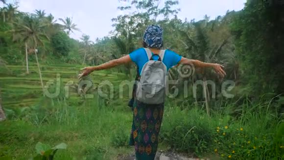 穿着休闲蓝色服装的俄罗斯女旅行者站在印度尼西亚一望无际的田野中间站在上升的地方视频的预览图