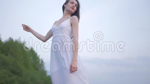 一位美丽快乐的年轻女子穿着白色连衣裙棕色长发在春天温柔而感性的时尚肖像视频的预览图