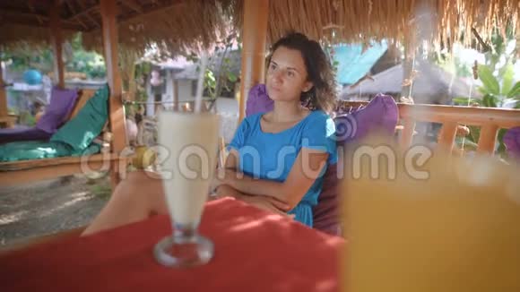年轻漂亮的黑发女郎正坐在桌子旁的热带岛屿酒吧里享受她的假期女性旅行者视频的预览图