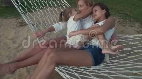 小女孩在吊床上轻轻拥抱着妈妈和妹妹视频的预览图