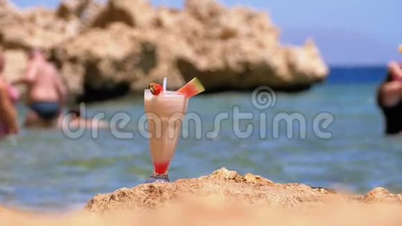 埃及海滩上的一种带稻草的玻璃中的热带鲜榨果汁矗立在海边的岩石上慢动作视频的预览图