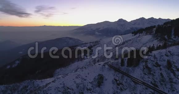 在冬季雪山道路上行驶的带有前照灯的汽车前俯视黄昏或黎明视频的预览图