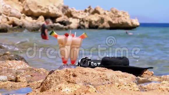 埃及海滩上的一种带稻草的玻璃中的热带鲜榨果汁矗立在海边的岩石上慢动作视频的预览图