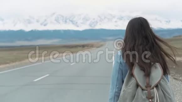 年轻女子在田野的路上搭便车年轻女孩嬉皮士在路上搭便车在山里视频的预览图