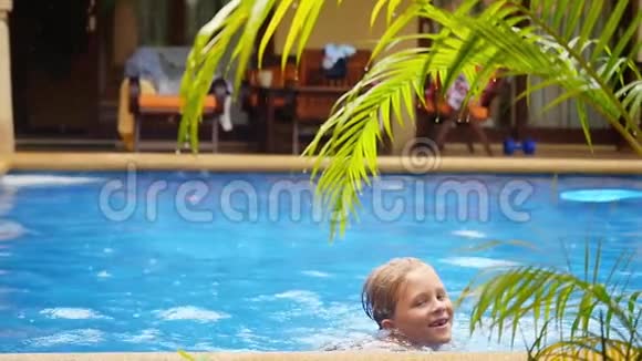 兴奋的微笑男孩在雨中用棕榈树的树枝泼水的游泳池里游泳慢动作1920x1080视频的预览图