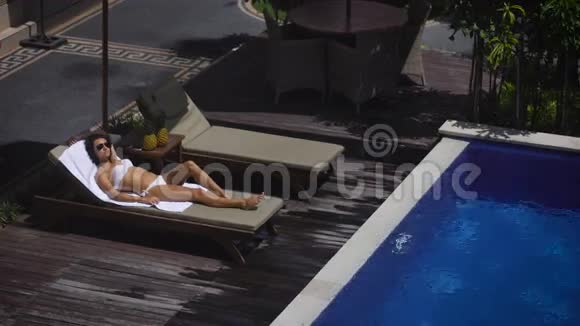 酒店的领地那个穿白色泳衣的女孩躺在游泳池旁的休息室里它会放松下来视频的预览图