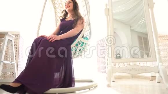 穿紫色衣服的漂亮女孩坐在豪华内部的圆形藤椅上视频的预览图
