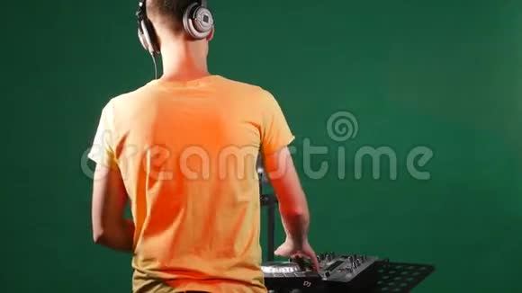 dj混合音乐站在他的甲板上在他的耳机里跳舞从后面视频的预览图