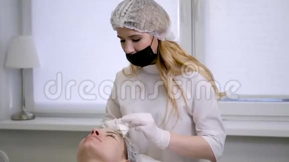 医生美容师从他躺着的病人脸上取出白色的奶油视频的预览图