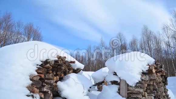蓝天上的轻云层移动着有着移动的桦树和覆盖着大雪的柴堆视频的预览图