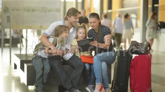 一个大家庭的成员坐在机场或机场的候机室里在平板电脑上观看度假照片视频的预览图