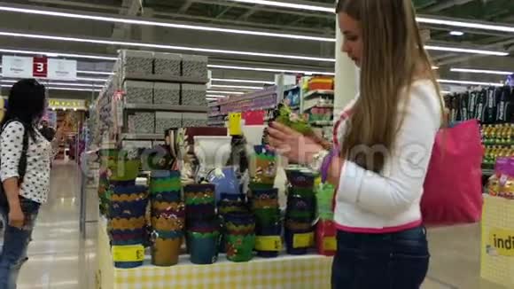 年轻女子选择超市里的花盆在背景中一个女人吃冰淇淋视频的预览图