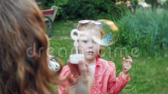 快乐妈妈和她的小女儿一起在户外玩耍吹肥皂泡在后院玩得很开心大自然视频的预览图
