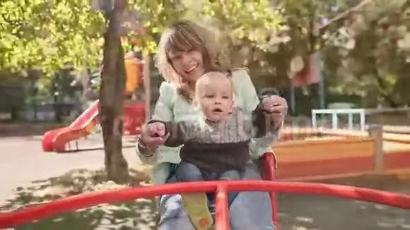 年轻快乐的母亲和婴儿在绿色公园的旋转木马上视频的预览图