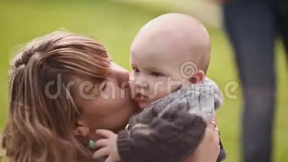 绿色草坪上美丽的妈妈和宝宝妈妈亲吻宝宝玩他视频的预览图