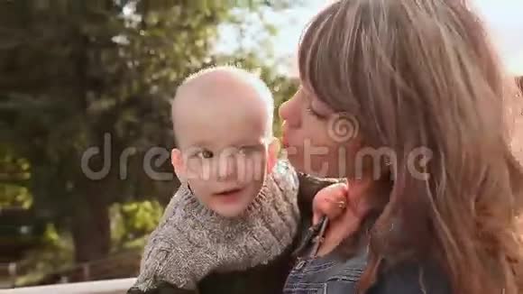 年轻漂亮的母亲抱着一个婴儿母亲在大自然上拥抱和亲吻儿子视频的预览图