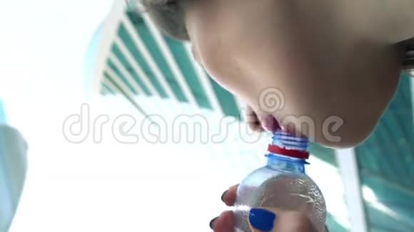 小女孩从小瓶子里喝水靠摩天大楼4K近景从下面看视频的预览图