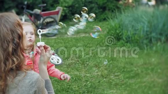 快乐妈妈和她的小女儿一起在户外玩耍吹肥皂泡在后院玩得很开心大自然视频的预览图