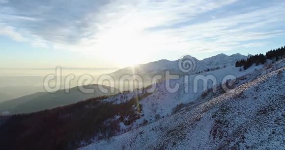 在日落或日出时在冬季雪山和树林上向前鸟瞰黄昏或黎明的阳光视频的预览图