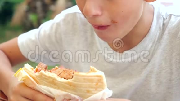 一个有魅力的男孩坐在一家快餐店里吃一个新鲜的面包皮塔里面有新鲜的蔬菜和肉沙拉视频的预览图