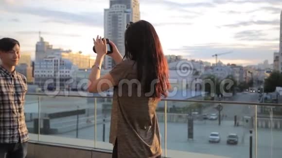 亚洲学生在城市户外为一名混合种族女孩摄影师摆姿势摄影技术的后台视频的预览图