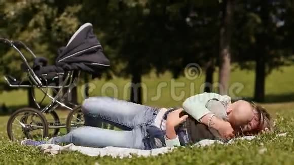 快乐的年轻妈妈在草坪上和婴儿玩耍亲吻她的儿子视频的预览图