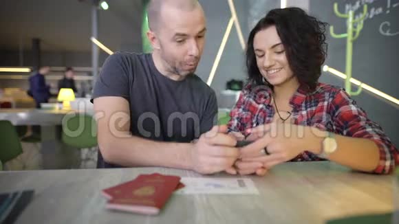 年轻夫妇坐在桌子旁用手指点击智能手机屏幕男子和妇女视频的预览图