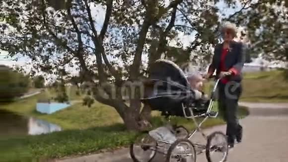 年轻快乐的祖母和我的小孙子一起散步坐在轮椅上背景是一片草地和一座教堂视频的预览图