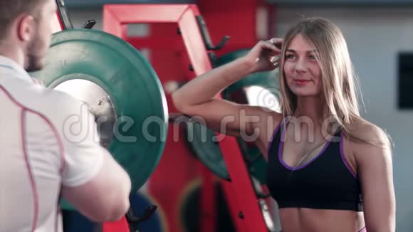 体育男向健身房里的金发女人展示他的二头肌视频的预览图