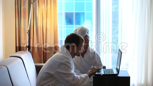 夫妻男人和女人在淋浴后坐在酒店房间的沙发上看着笔记本电脑视频的预览图