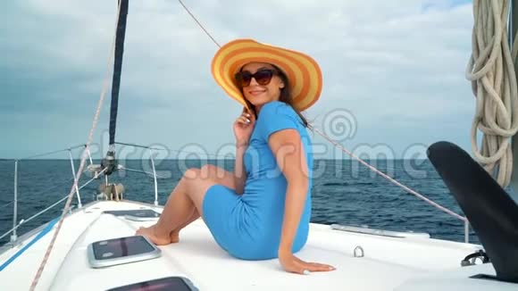 戴着黄色帽子的女人和穿着蓝色衣服的女孩在海洋的夏季在游艇上休息慢动作视频的预览图