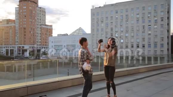 亚洲学生在城市户外为一名混合种族女孩摄影师摆姿势摄影技术的后台视频的预览图