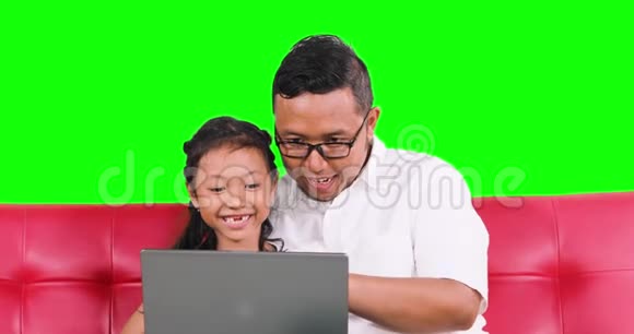 开朗的父亲和女儿在沙发上用笔记本电脑视频的预览图