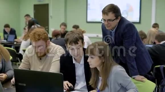 一群穿着休闲和商务服装的人坐在办公桌前在控制下使用笔记本电脑视频的预览图